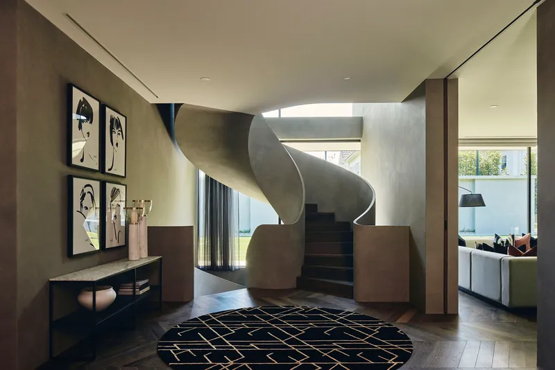Sculptural spiral staircase in blackened steel rising through a skylit void in the entry hall