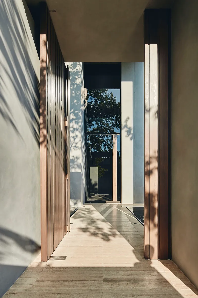 Entry corridor with dappled sunlight filtering through trees onto timber cladding and concrete walls