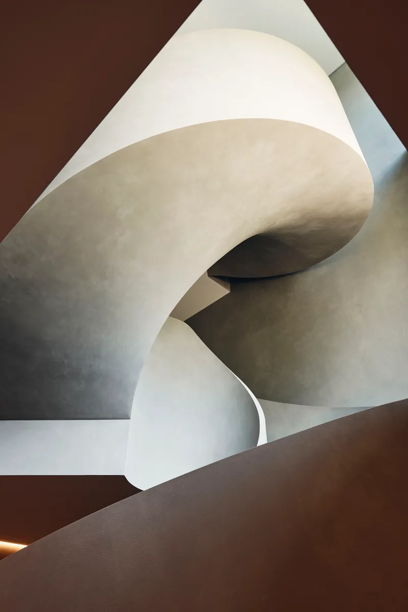 View upward through the stairwell showing layered curved plaster forms and shadow