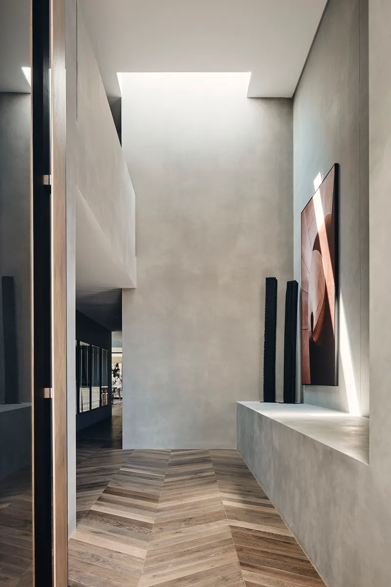 Corridor with herringbone timber floor, skylight above, and concrete bench displaying sculptures