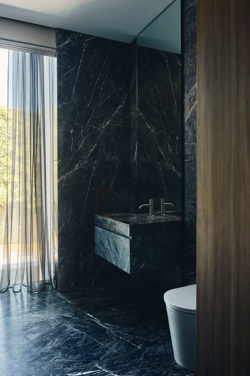 Bathroom with black marble walls, floating sink, and sheer curtains revealing trees outside