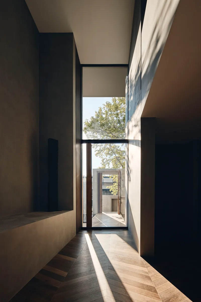 Hallway with tall glazed door framing a courtyard view and timber flooring in afternoon sun