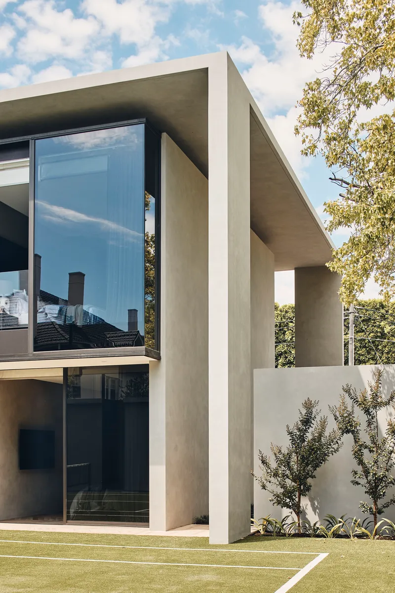 Exterior corner showing deep concrete frame around glazing with olive trees and lawn