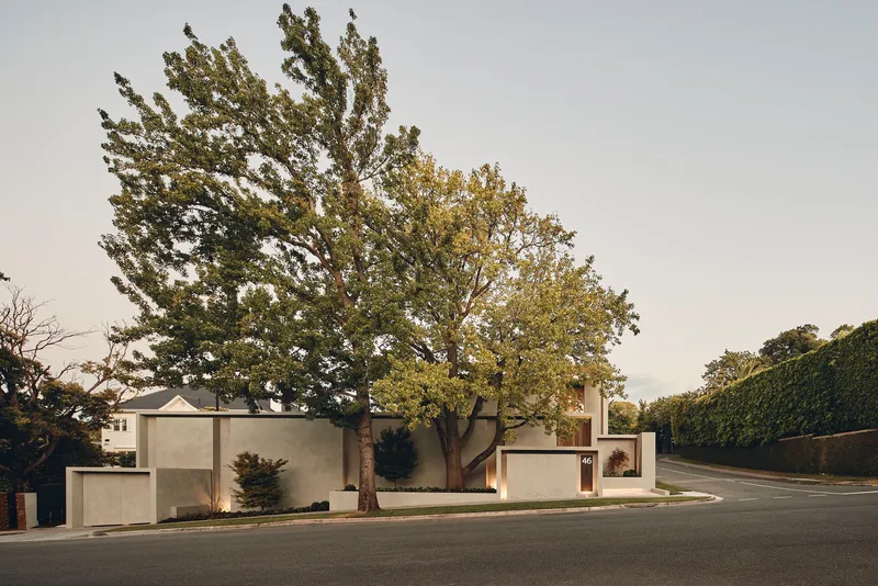 Street view showing the stacked concrete volumes framed by mature trees under an overcast sky