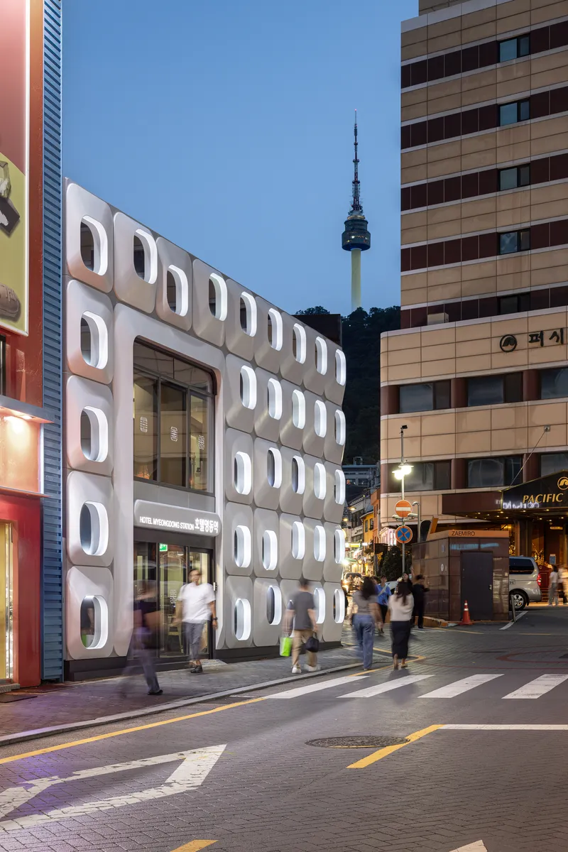 White modular facade with circular porthole windows under evening sky with communications tower visible