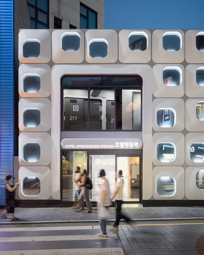 Entry facade with stacked porthole modules and pedestrians crossing at street level in motion blur