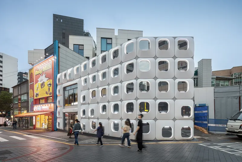 White modular facade with rounded square windows on a busy street corner at dusk