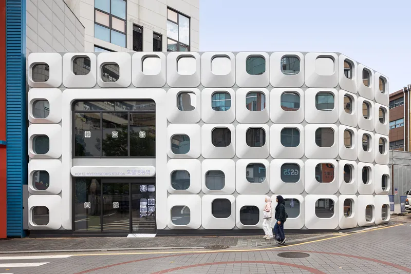 Street level view of white modular facade with rounded square windows as a pedestrian walks by