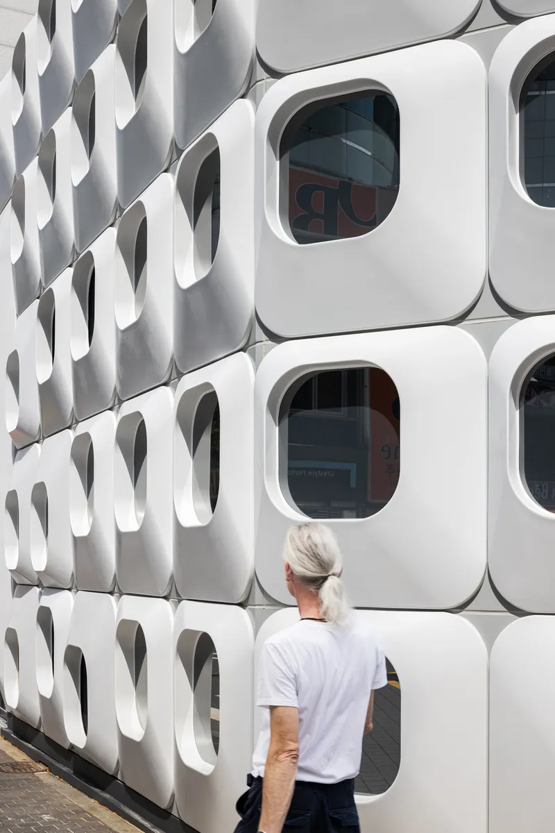 White modular facade with rounded square windows and a person in a white shirt looking up