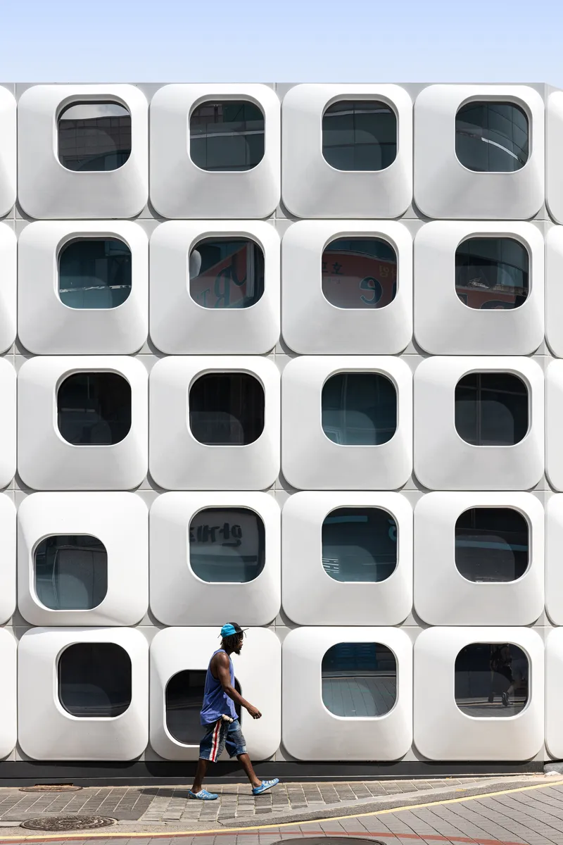 Grid of rounded square window modules with a person walking past on the pavement below
