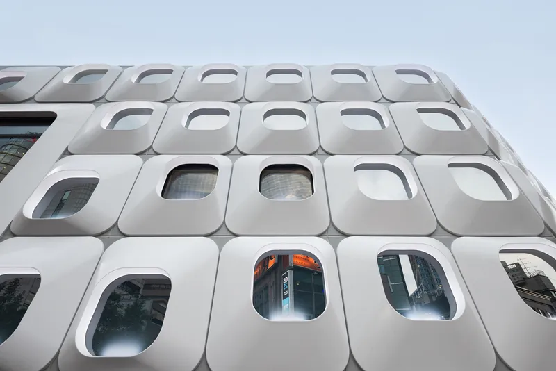 Upward view of the white modular facade with rounded square openings against an overcast sky