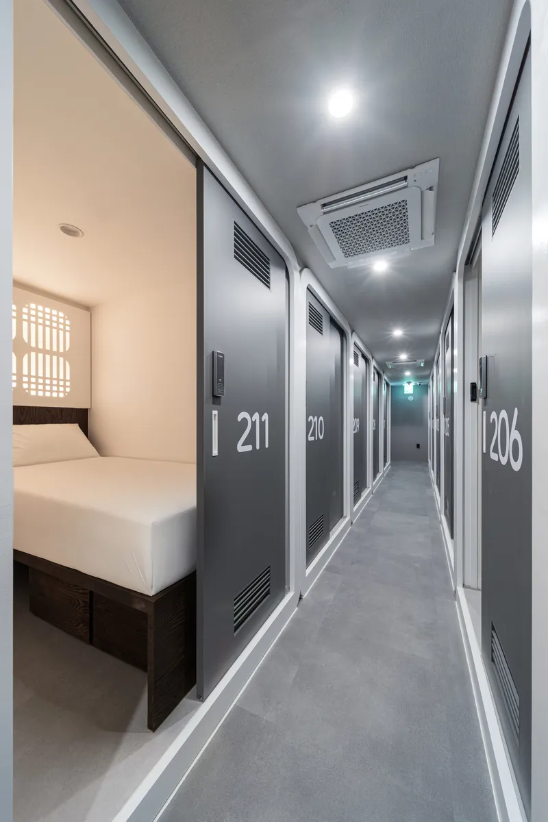 Interior corridor with numbered grey doors and recessed ceiling lights leading to a sleeping capsule