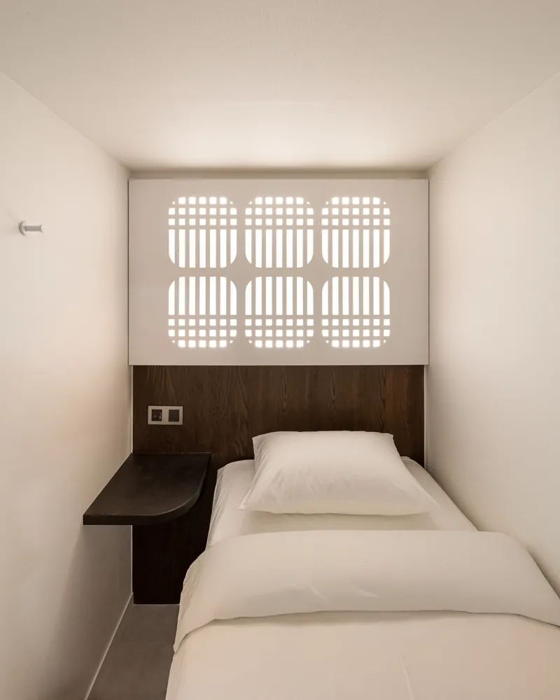Compact sleeping room with dark wood headboard and geometric perforated screen above the bed