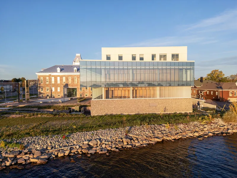 Waterfront elevation with glass curtain wall above a gabion stone base at golden hour