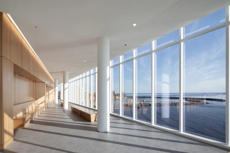 Interior corridor with floor-to-ceiling glazing overlooking the harbor and timber-clad wall with integrated seating