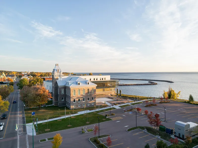 Aerial view of the glass and stone complex along a waterfront with autumn trees and parking lot