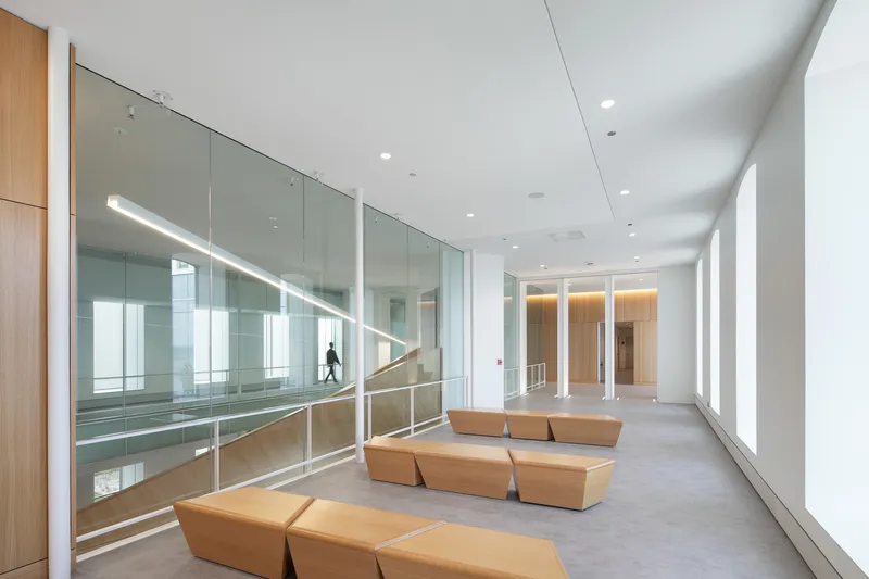 Upper-level corridor with orange modular seating and glazed balustrade overlooking the atrium below
