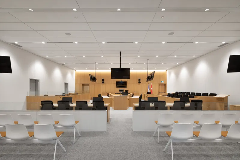 Courtroom interior with timber judicial bench, black monitors, and rows of gallery seating under recessed lighting