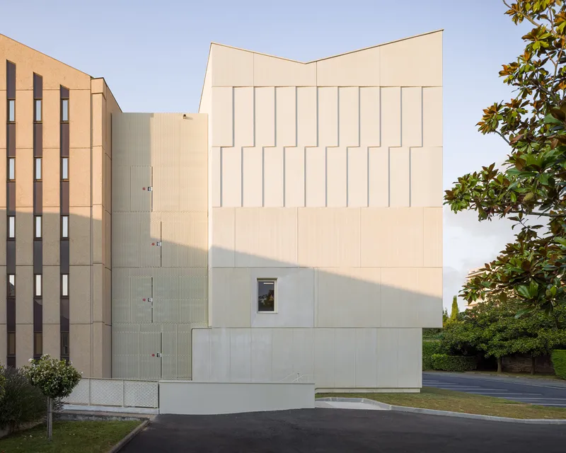 Rear elevation showing the faceted white facade in warm afternoon light with adjacent residential tower