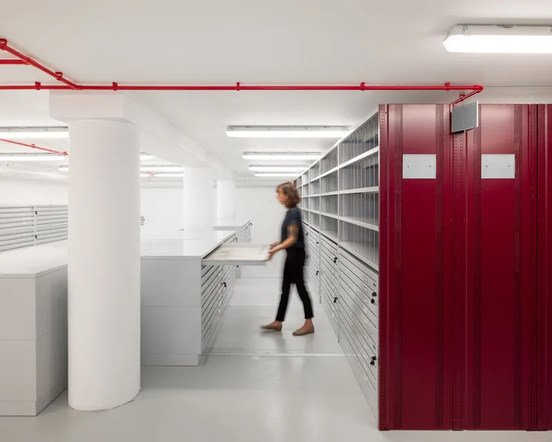Interior archive room with red mobile shelving units and white storage cabinets as figure walks through