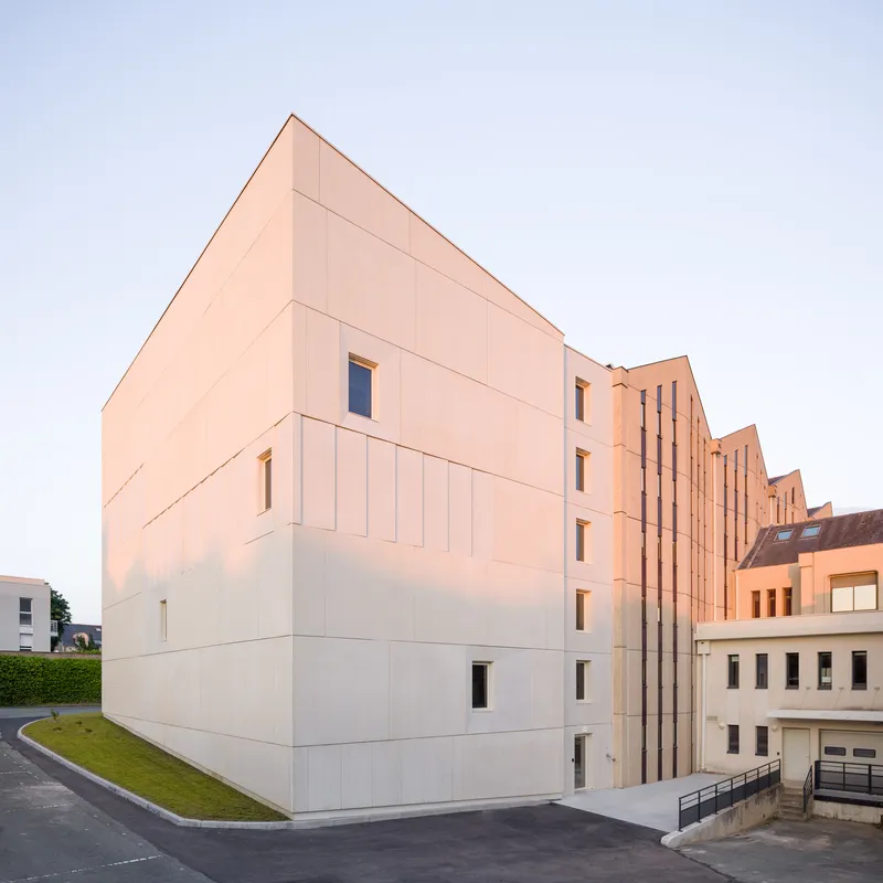 Stepped sawtooth volume clad in pale panels catching warm evening light beside an access ramp