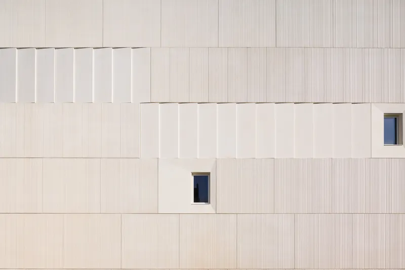 Facade detail showing vertically striated panels with offset joints and two small rectangular window openings