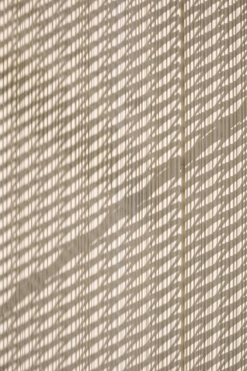 Dappled sunlight casting diagonal shadow patterns across a textured beige wall surface