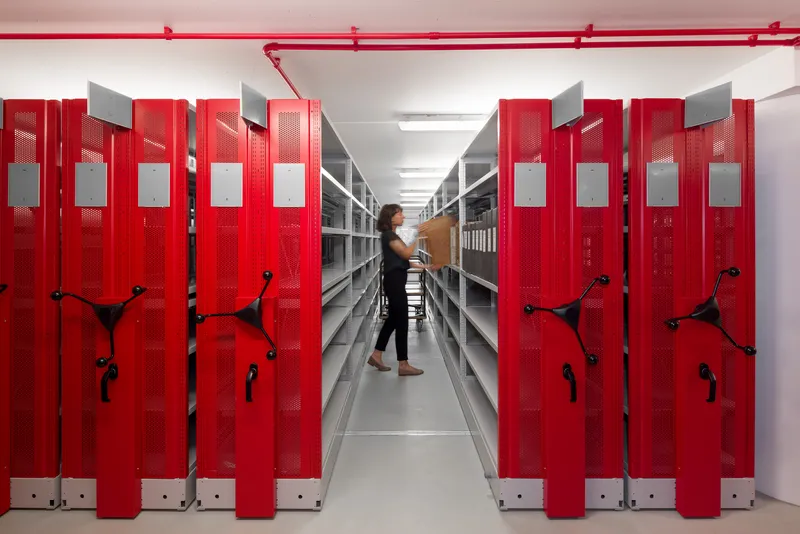 Aisle view of red mobile shelving units with perforated panels as a person walks through