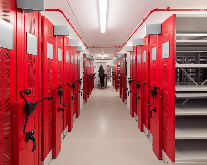 Red mobile shelving corridor with exposed conduit on ceiling and person in distance