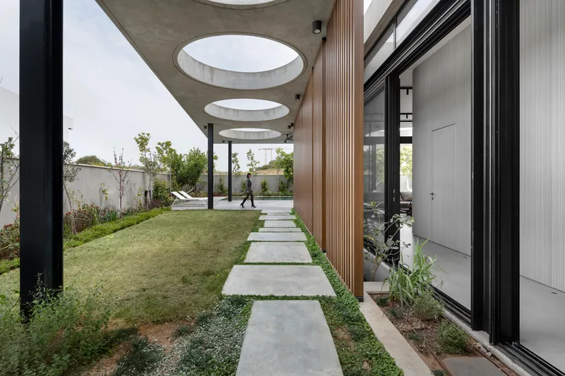 Concrete pathway with circular skylights cut into the canopy ceiling as a person walks through