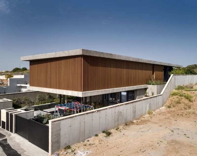 Elevated timber-clad volume on concrete base with terraced retaining walls on sloped terrain