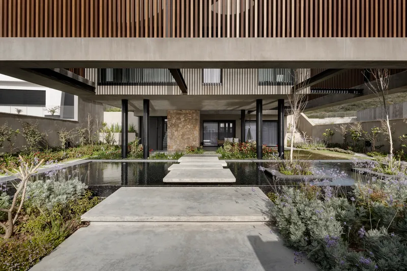 Entry pathway bridging reflecting pools beneath slatted timber soffit and black steel columns