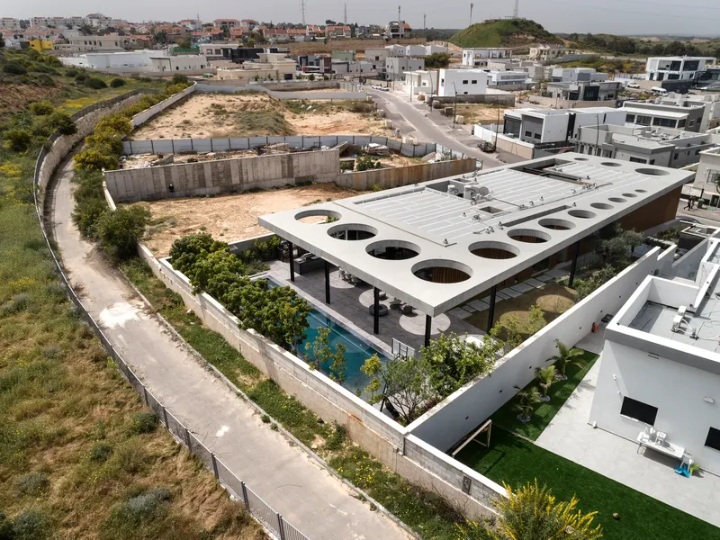 Aerial view of white concrete roof with circular voids over terraced gardens in hillside neighborhood
