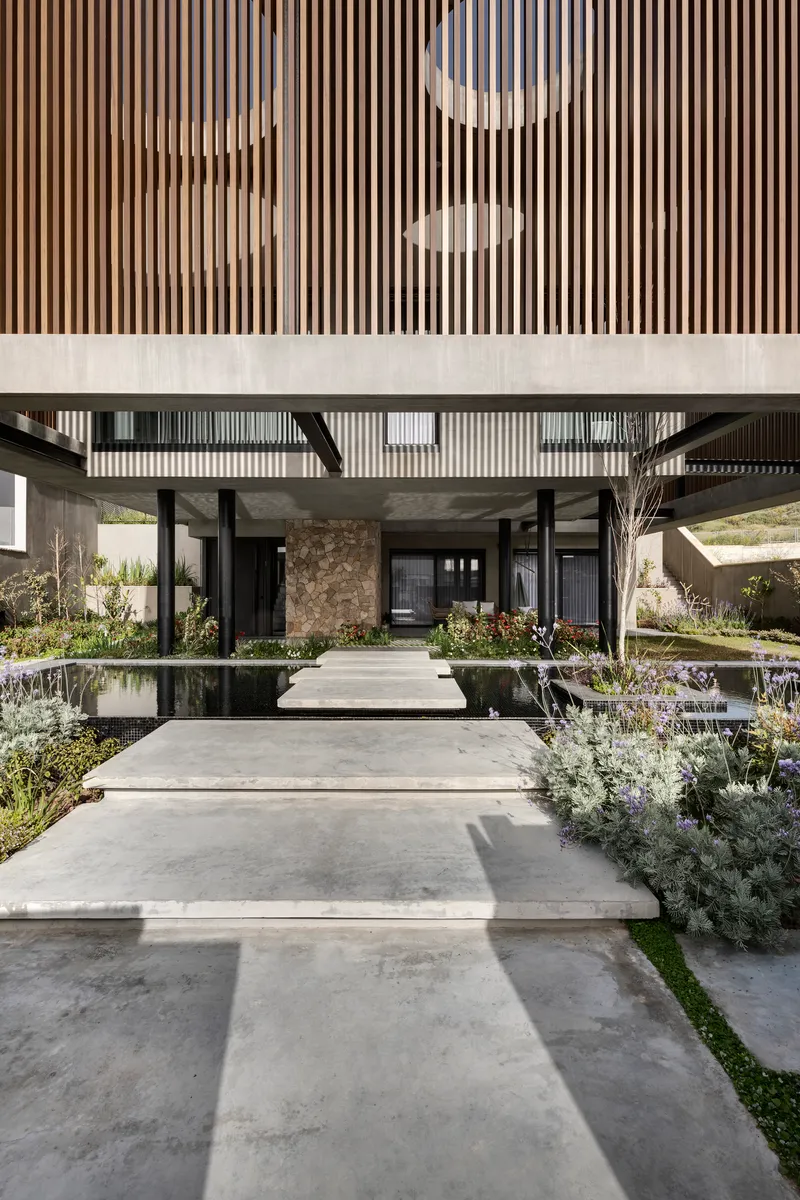 Covered entry courtyard with concrete stepping stones crossing a reflecting pool flanked by planted beds