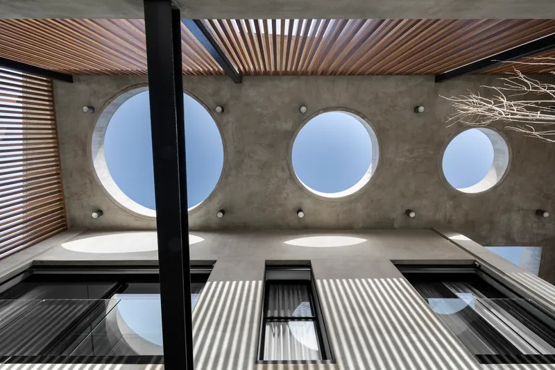 Upward view of concrete ceiling with circular skylights and timber louvered screens casting shadow patterns
