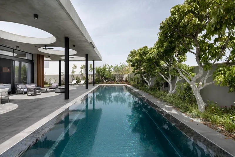 Long lap pool bordered by paving and mature trees under a concrete canopy with circular skylights