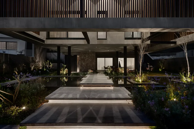 Illuminated entrance pathway with reflecting pools flanking concrete stepping stones at dusk