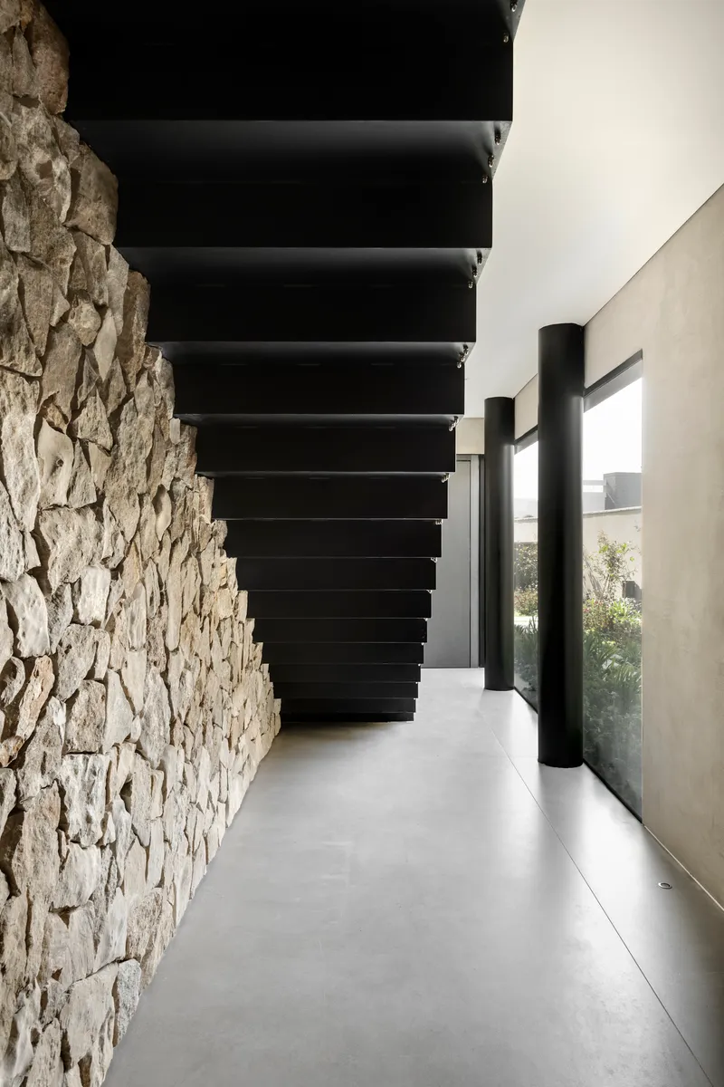 Corridor with stone wall and floating black steel stair treads beneath a glazed opening