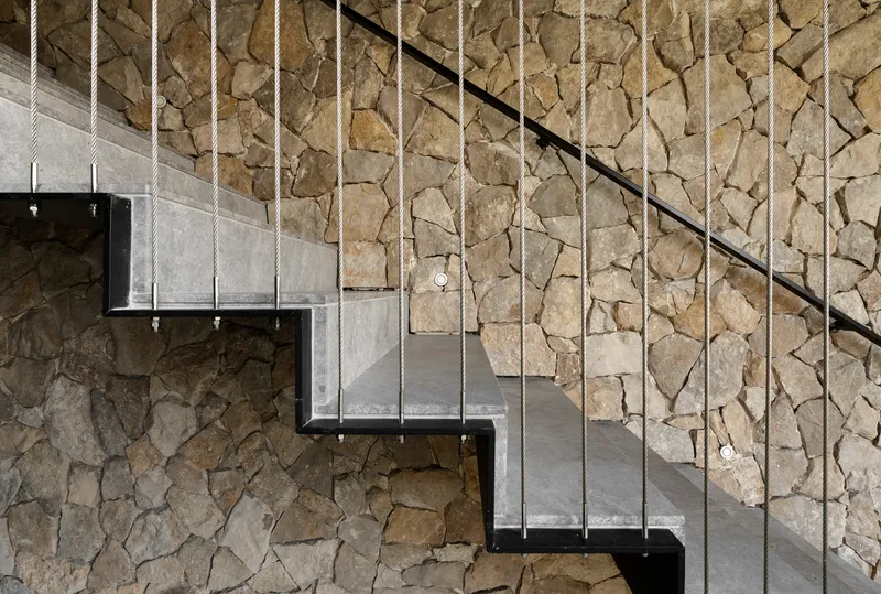 Detail of cantilevered concrete treads with steel supports and cable railing against stacked stone