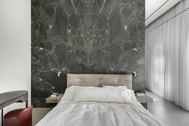 Bedroom with bookmatched grey marble headboard wall and sheer curtains filtering daylight