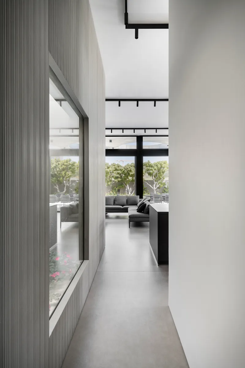 Narrow corridor with fluted grey wall panels and high clerestory windows overlooking a planted courtyard