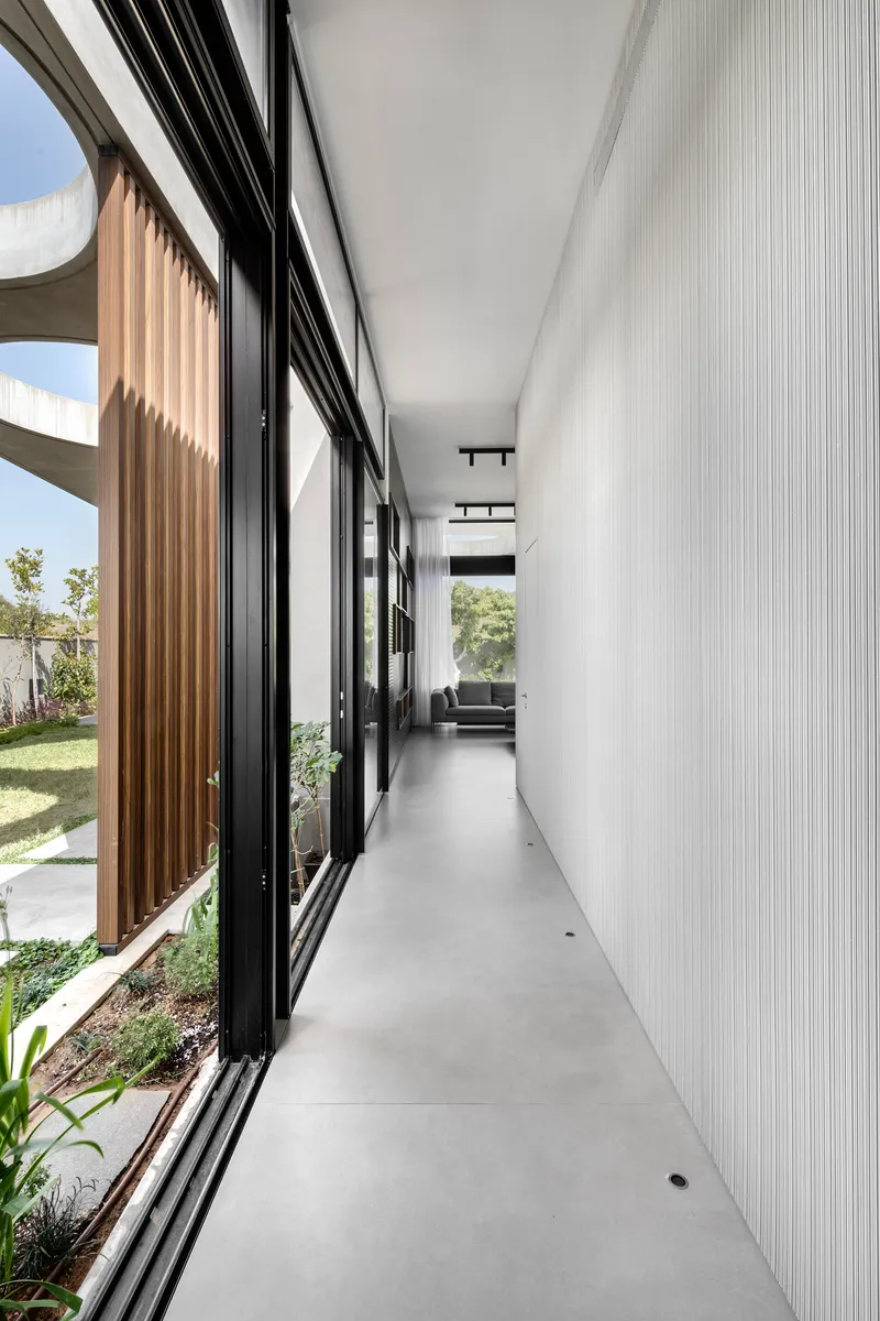Interior hallway with black-framed glazing and timber vertical screens filtering afternoon sunlight