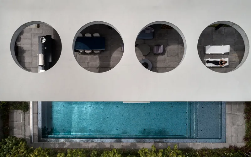 Overhead view of four circular openings in a white roof revealing interior spaces and a lap pool below