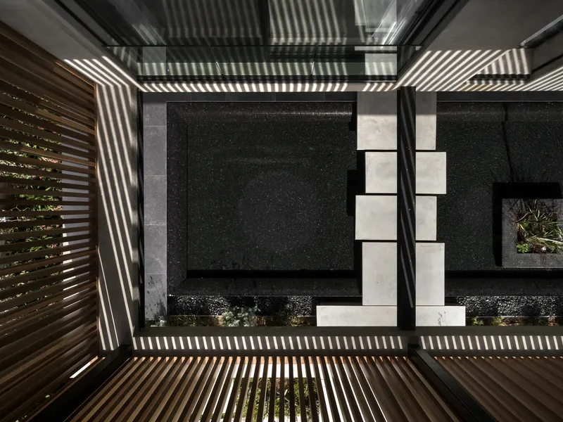 Looking up through a courtyard void showing horizontal slatted screens casting striped shadows across dark walls
