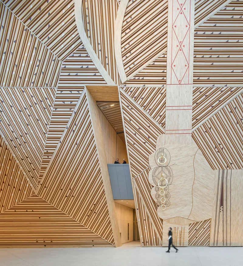 Interior atrium with chevron-patterned timber walls and ceiling with a person walking across the polished floor