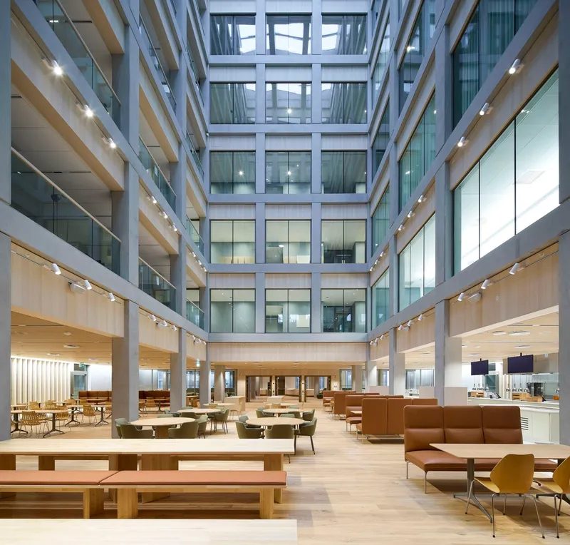 Multi-story interior atrium with timber balconies, glass railings and seating areas under a skylight