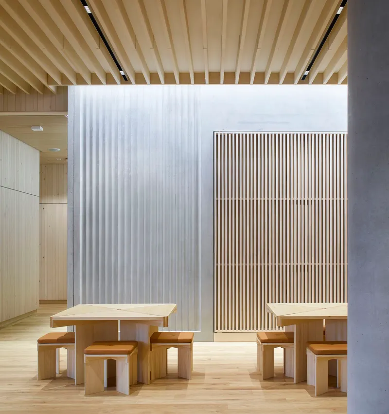 Reading area with timber benches and tables beneath a ribbed wood ceiling and translucent curtain