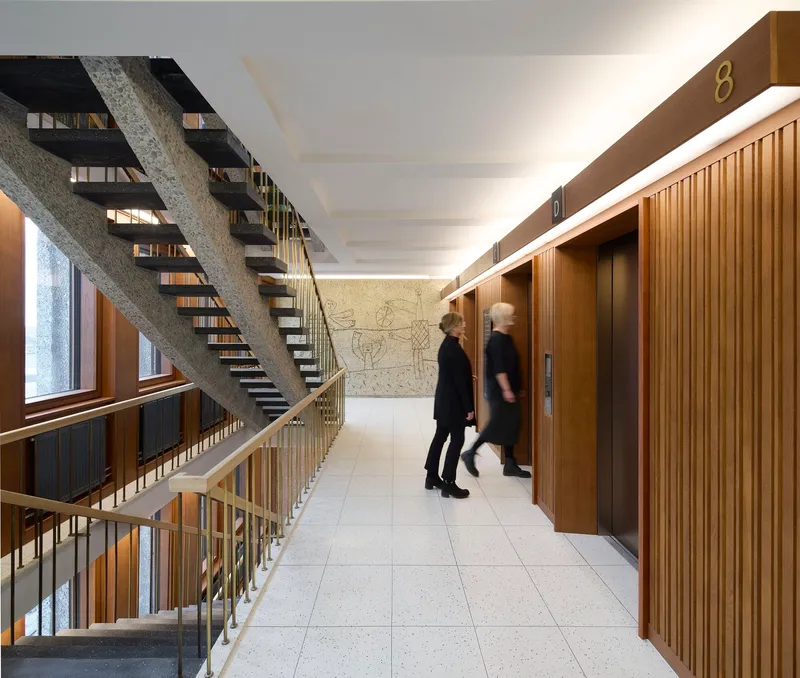 Elevator lobby with timber cladding and exposed concrete staircase with two people in motion