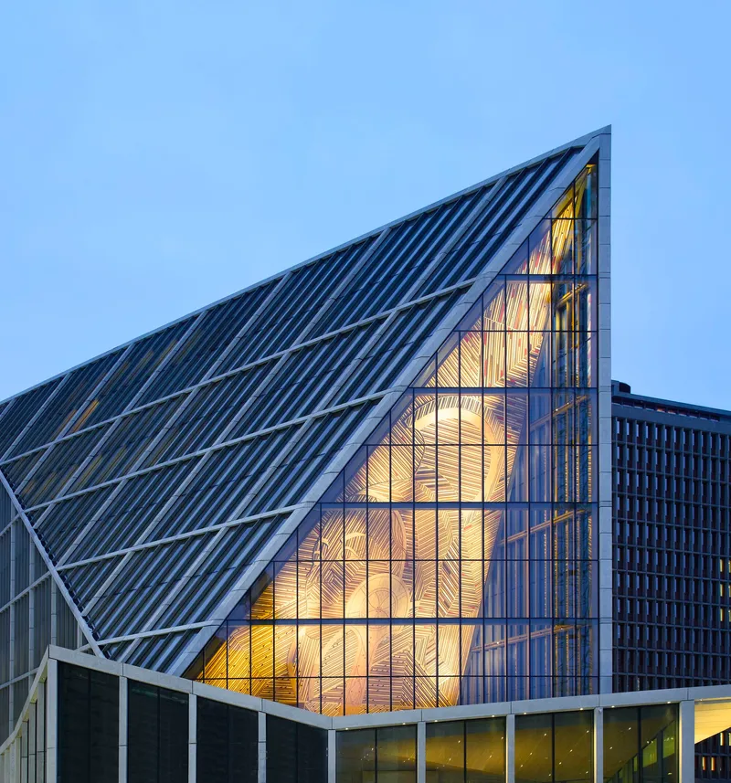 Triangular glass gable revealing illuminated timber-lined interior at twilight