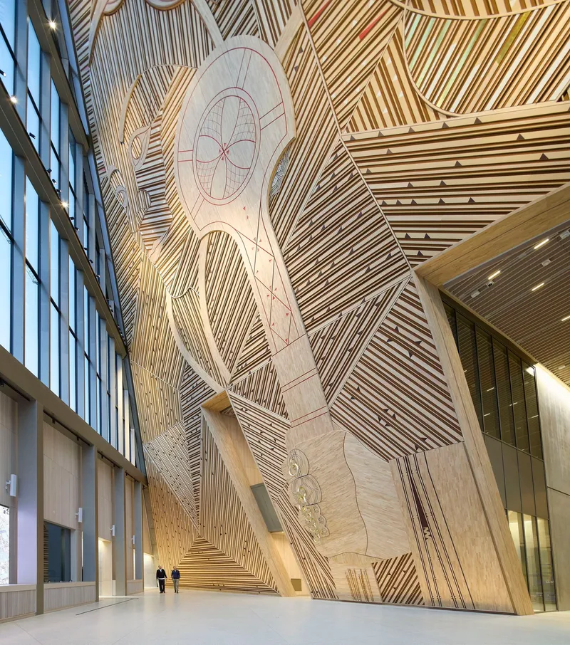 Towering atrium wall clad in wood slats arranged in diagonal patterns with carved figural reliefs